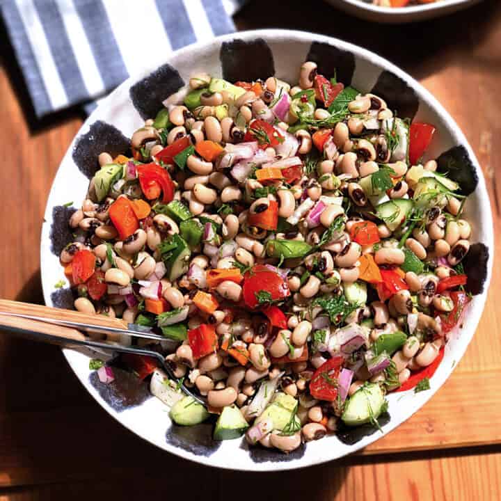 A bowl with black eye peas salad and serving utensils on a wood table.