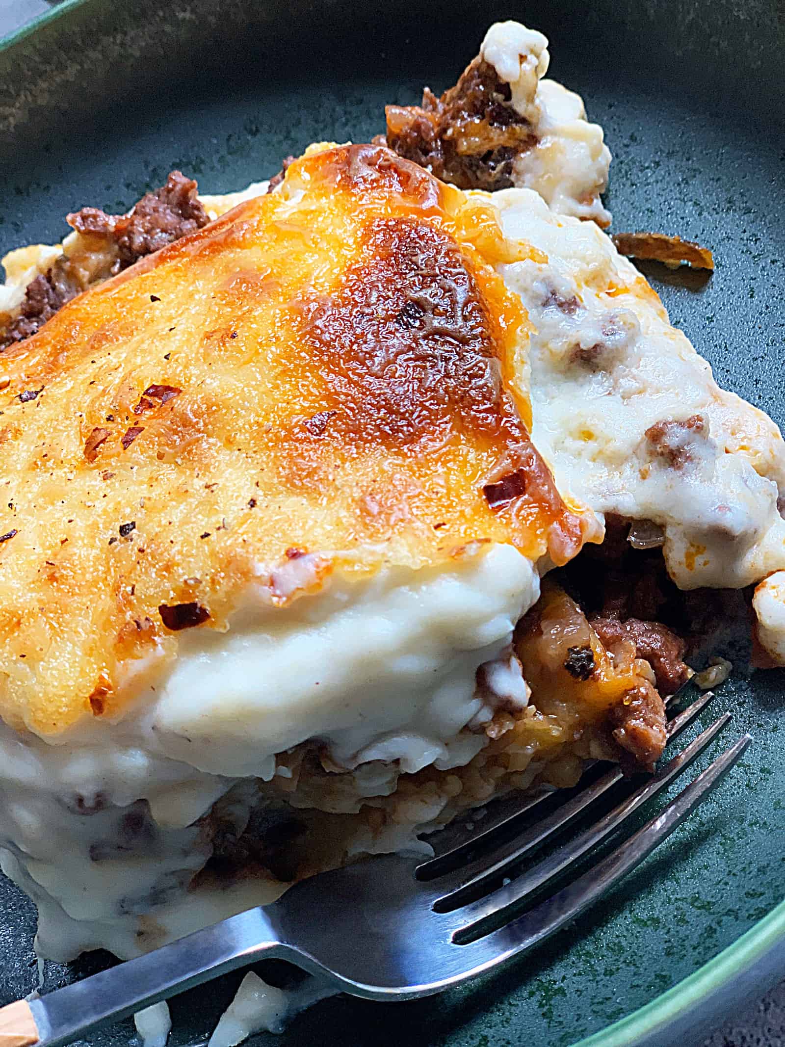 A green plate with a piece of vegetarian moussaka cooked with plant based meat Beyond beef.