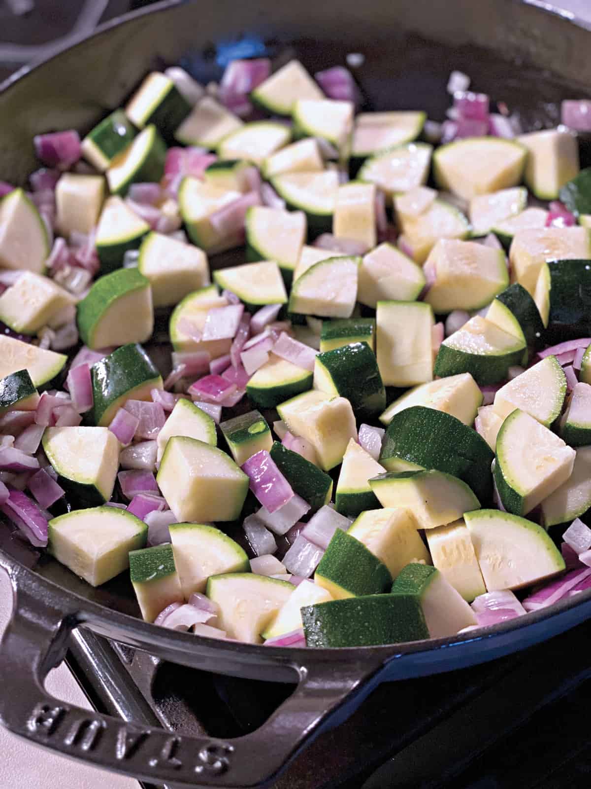 A pan with cubed zucchini and onions cooking.