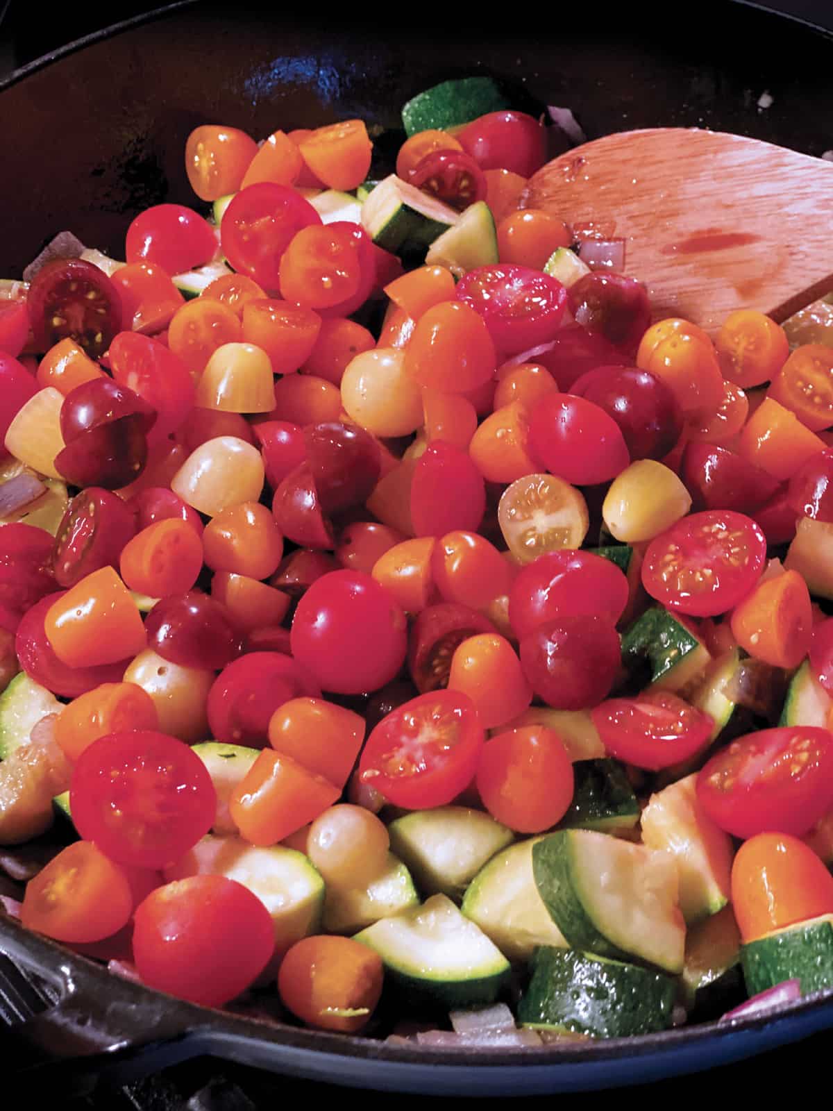 A pan with cubed zucchini, tomatoes and onions cooking.