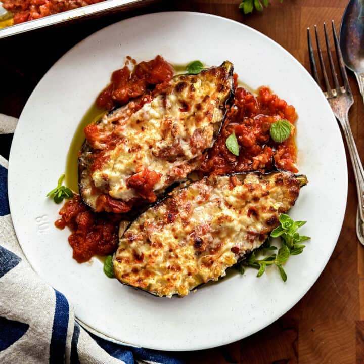 A plate with two stuffed eggplants and some herbs.