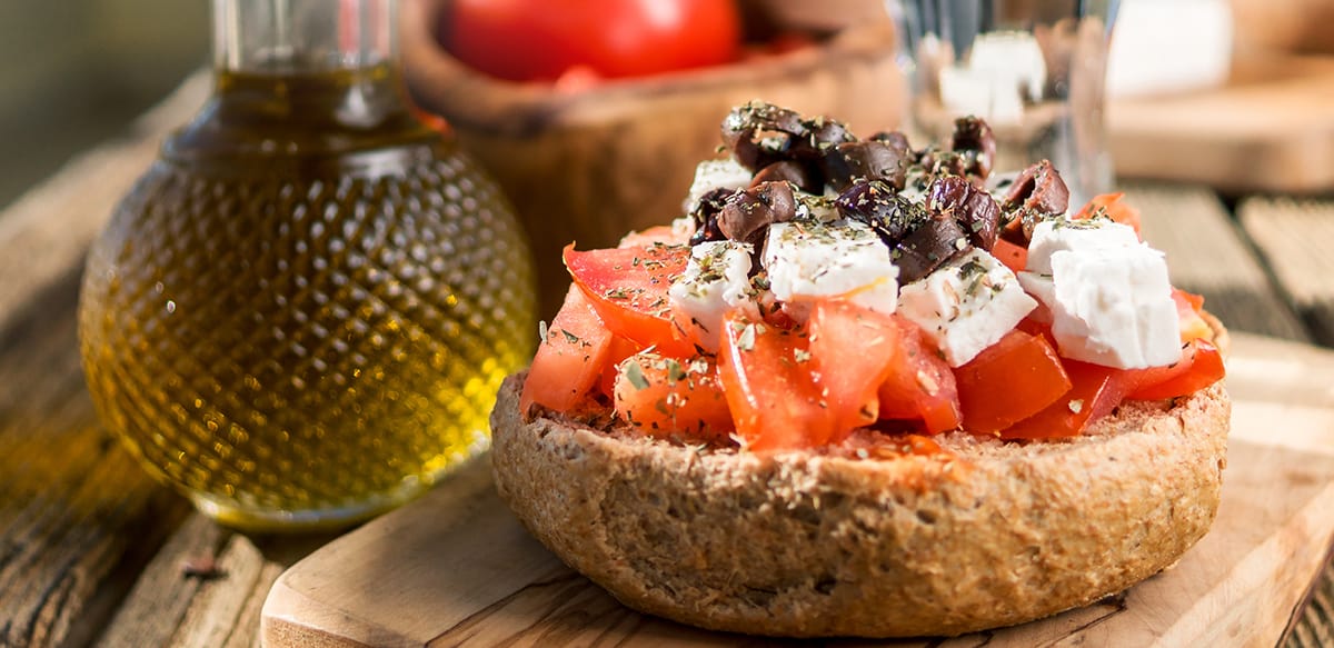 A cretan rusk with tomatoes, feta and olives on top. On the left a small glass bottle with olive oil.