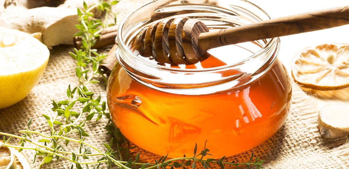 A jar with honey, fresh thyme sprigs  next to it.