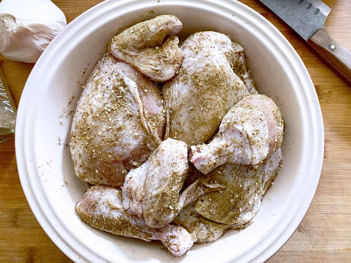 Raw chicken being marinated in a large bowl.