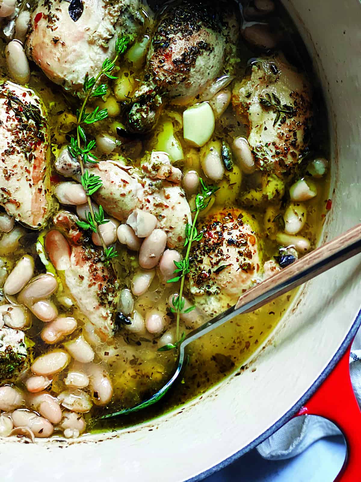 A red dutch oven with chicken stew with beans and a serving spoon.