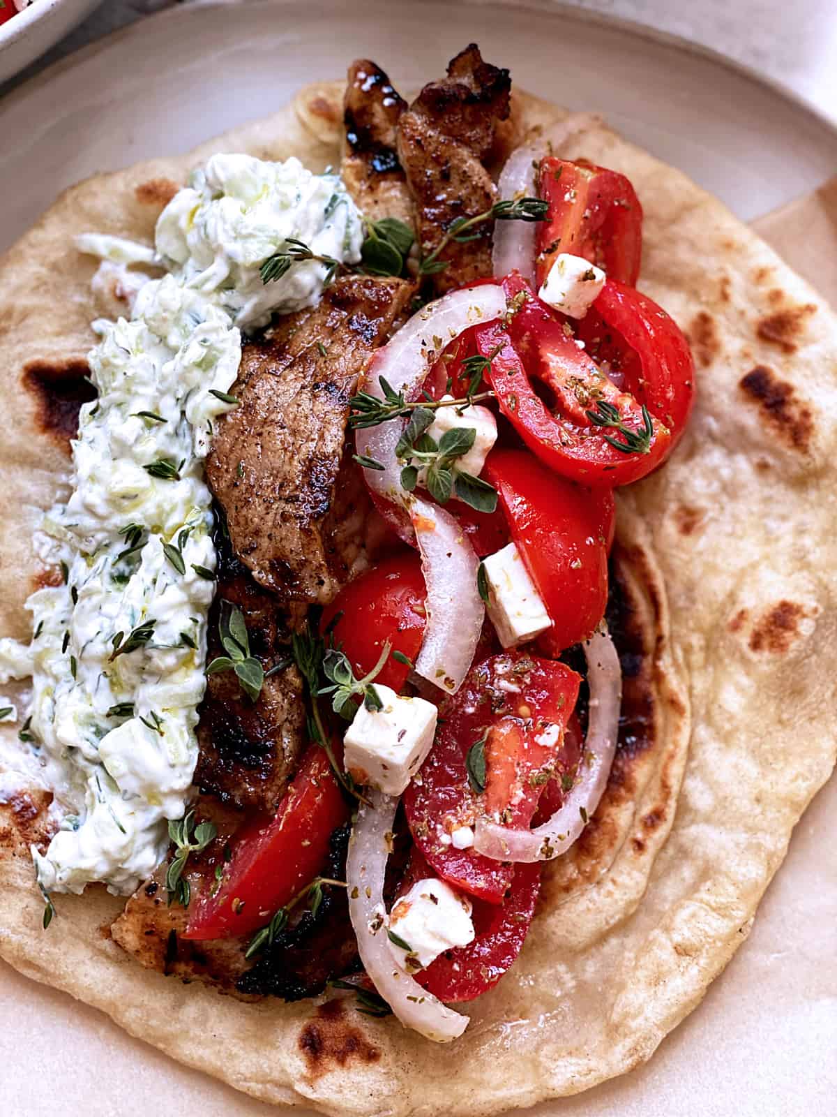 A plate with fillings for Greek souvlaki, a tzatziki bowl and tomato salad.