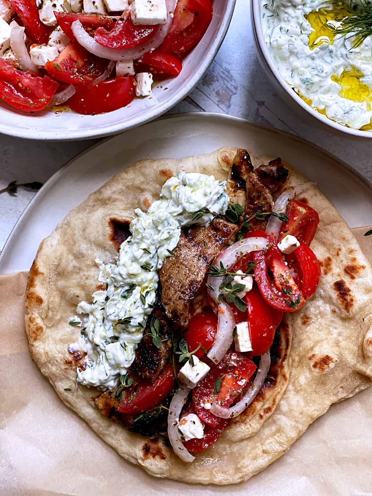 A plate with fillings for Greek souvlaki, a tzatziki bowl and tomato salad.