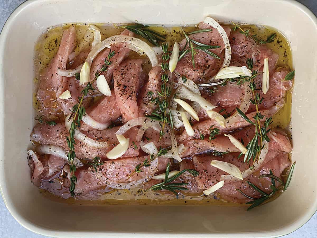 Pork marinating in olive oil with fresh herbs, onions and garlic.