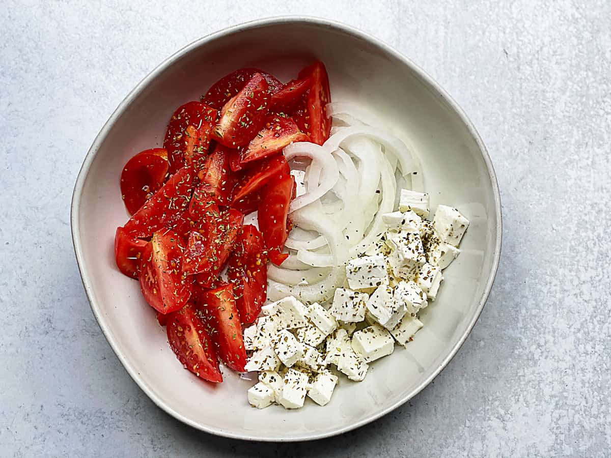 A bowl with tomatoes, onion and feta cheese.