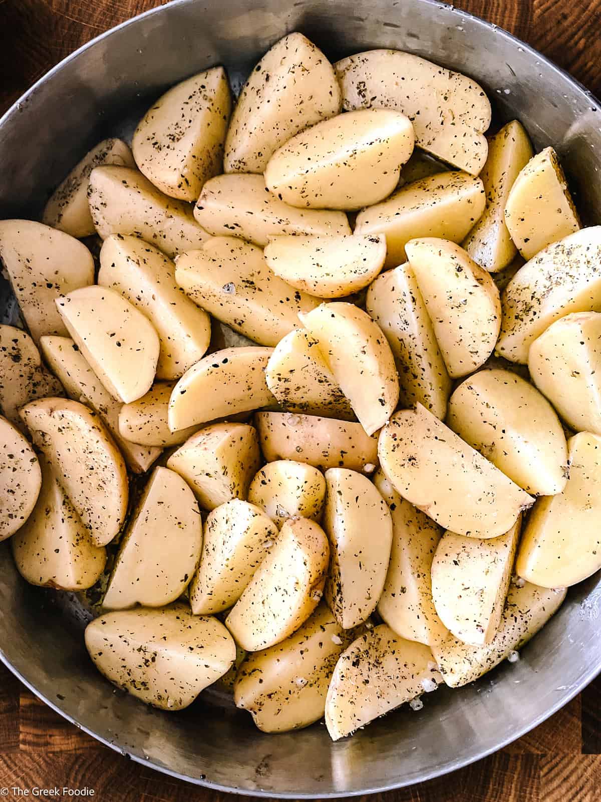 Yukon gold potato wedges tossed with olive oil, garlic and oregano in a baking pan, ready to roast.