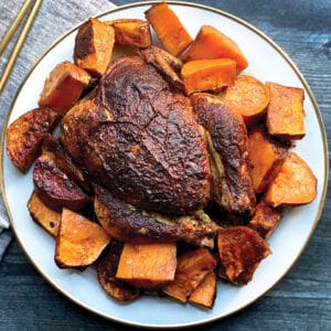 A roasted chicken with sweet potatoes on a plate.