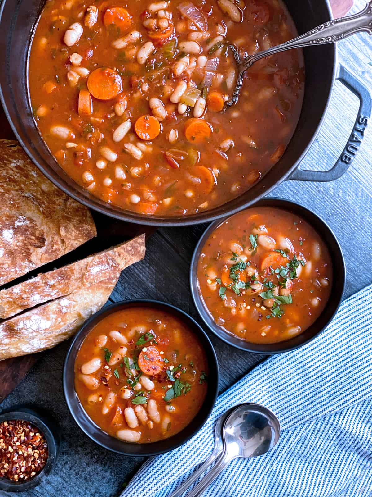 Two bowls with fasolada-greek white bean soup, bread and a pot filled with the soup.
