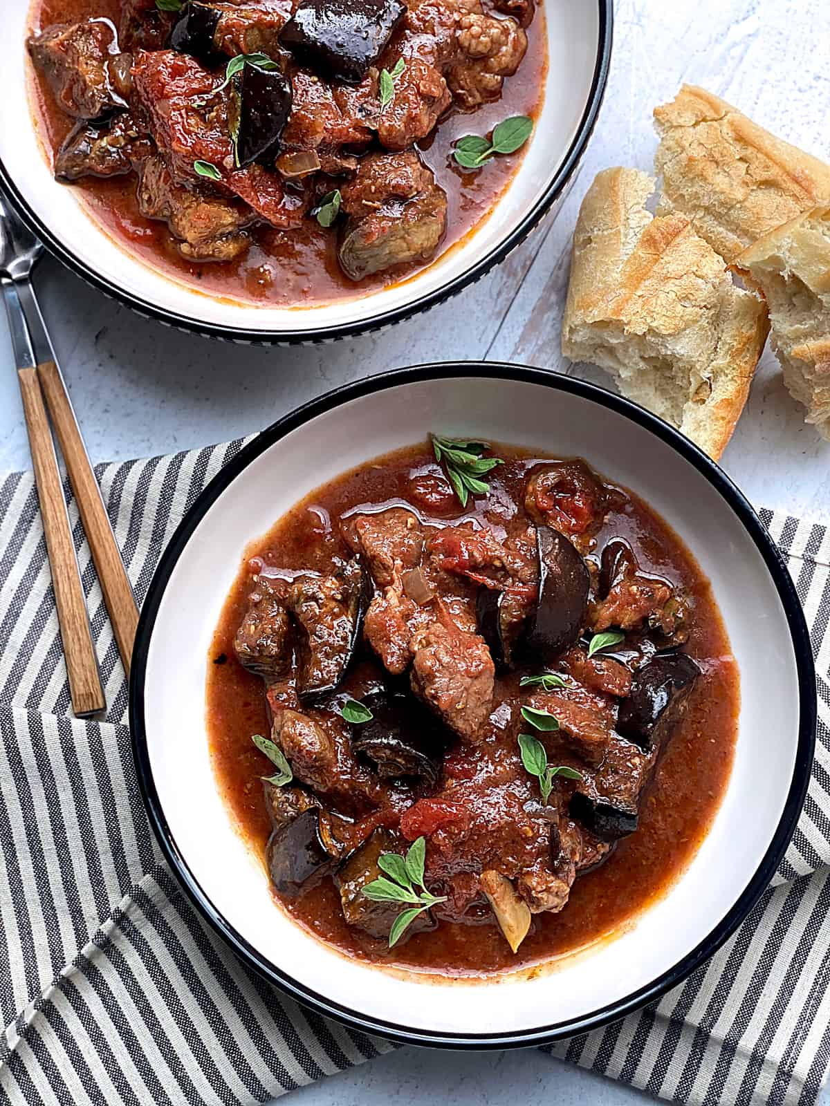 Two bowls with old fashioned beef stew and some pieces of bread, utensils and a napkin.