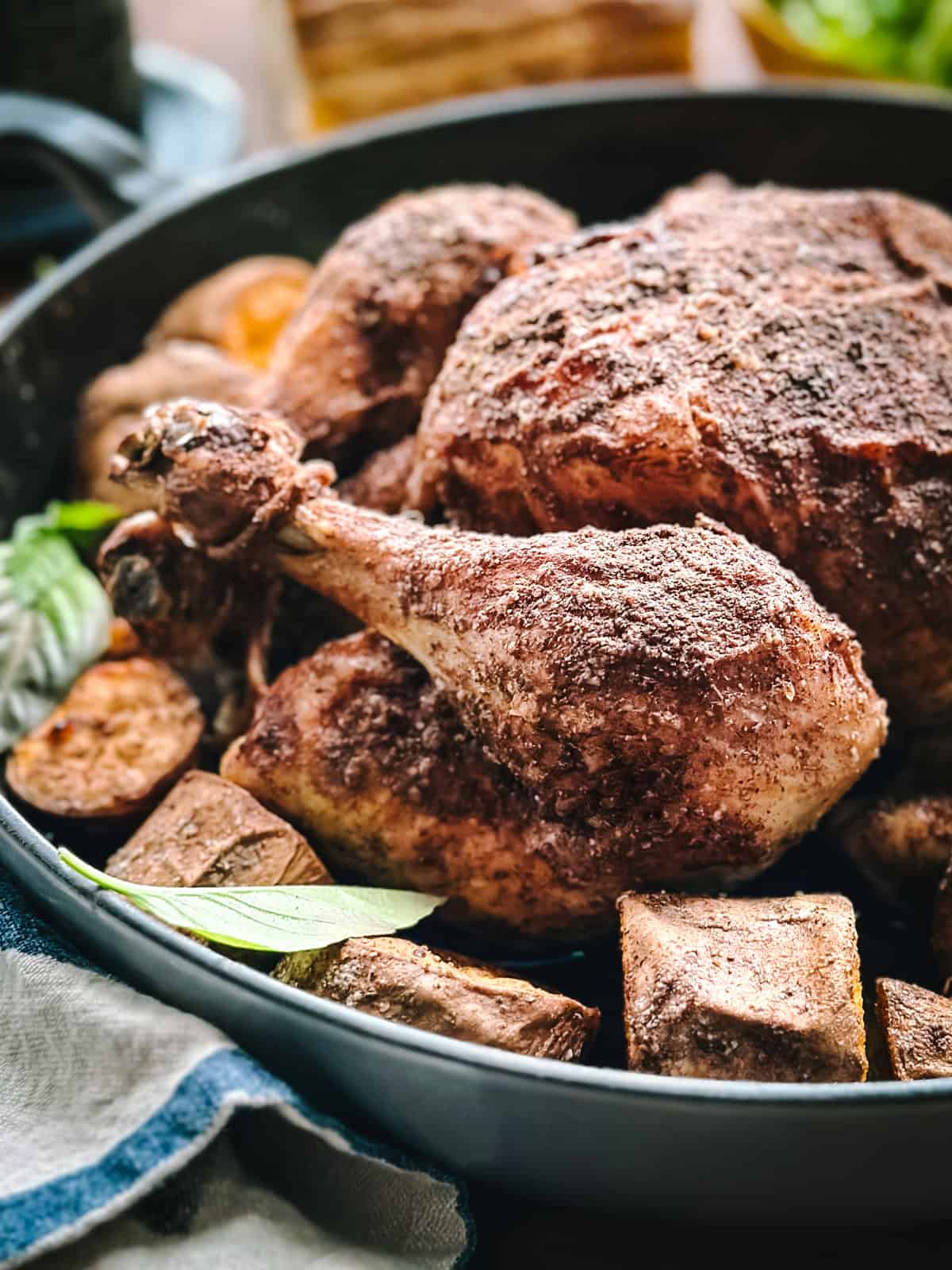 Close-up of roasted cinnamon chicken surrounded by caramelized sweet potatoes in a roasting pan.