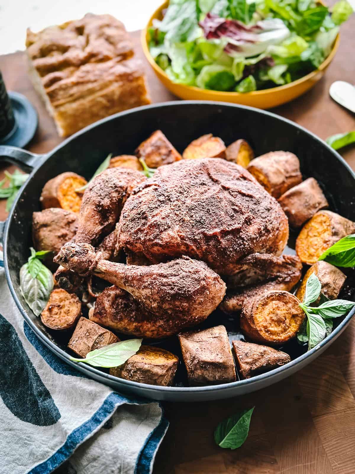 Golden roasted cinnamon chicken surrounded by caramelized sweet potato chunks in a roasting pan.