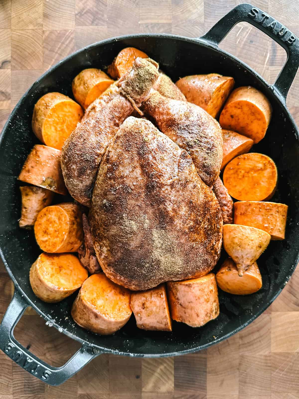 Whole chicken seasoned with cinnamon and cumin, packed with sweet potatoes in a roasting pan ready for the oven.