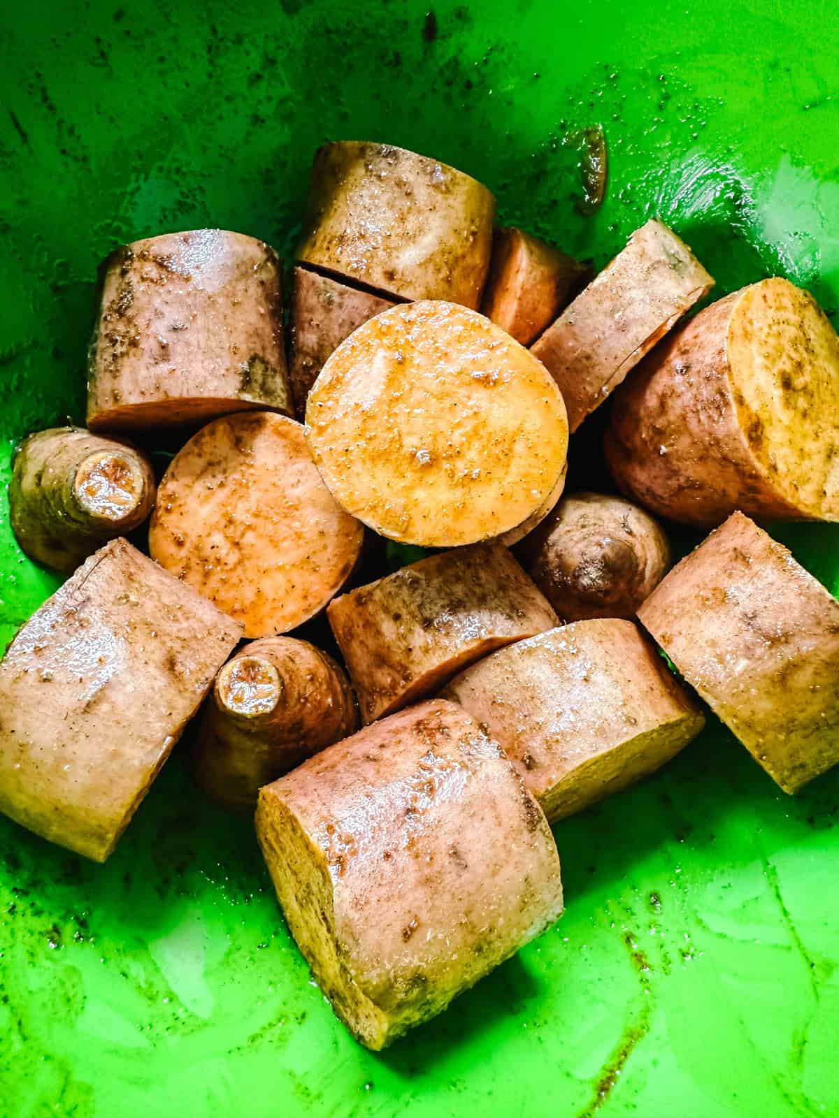 Sweet potato chunks tossed with cinnamon and olive oil in a bowl before roasting.