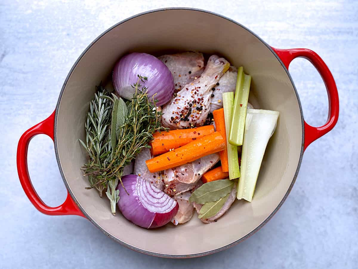 A red dutch oven with ingredients for chicken broth.