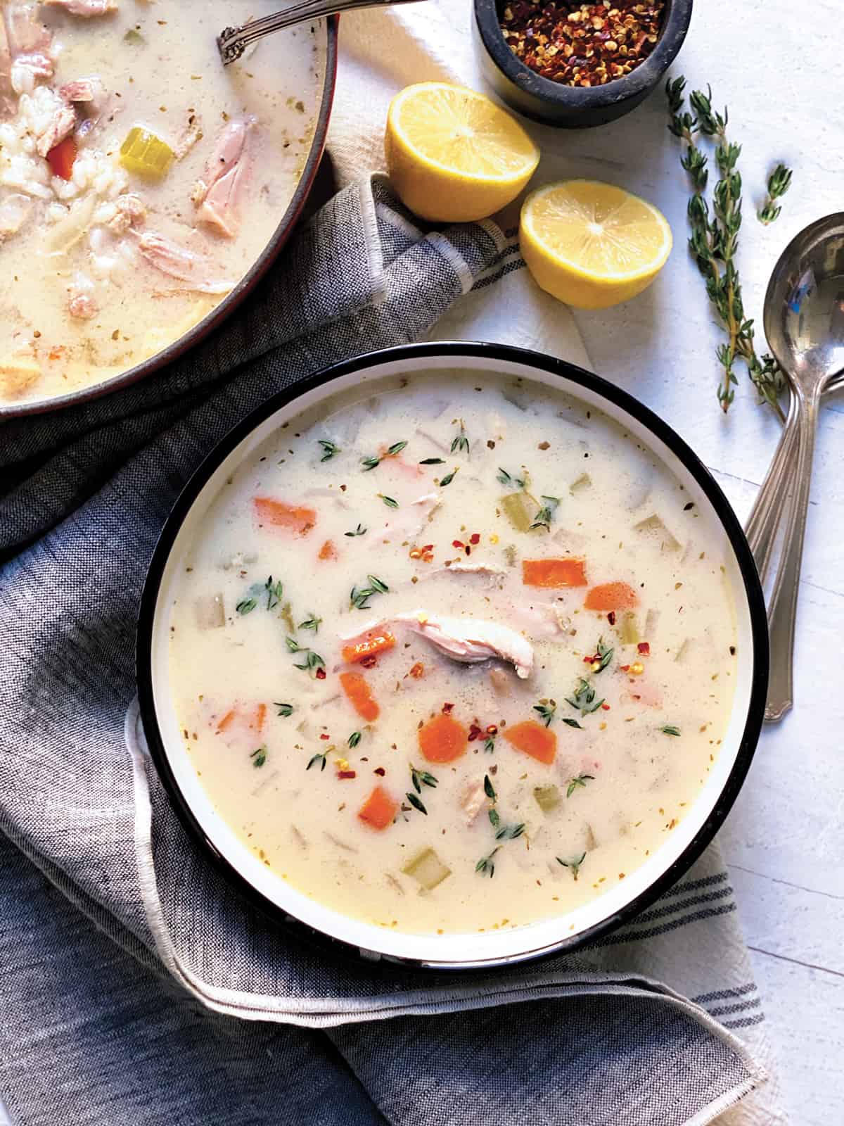 A red pot and a bowl with chicken soup, lemons and spoons.