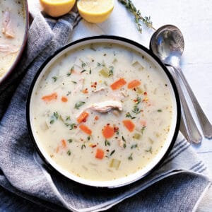 A bowl with greek chicken soup, a napkin and partial view of lemons and a stockpot with soup.