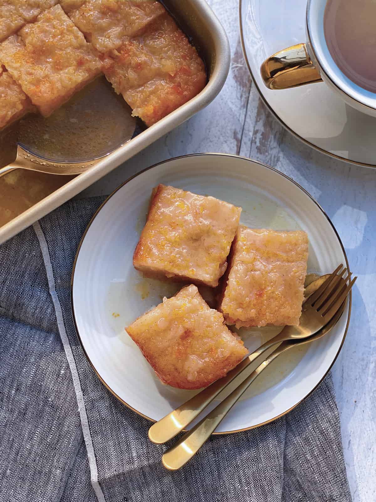 A plate with three pieces of greek orange phyllo cake utensils over napkin. A pan with cake at the back.