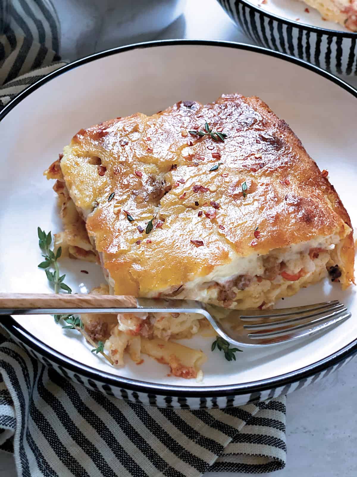A plate with a piece of Pastitsio-Greek lasagna and a fork.