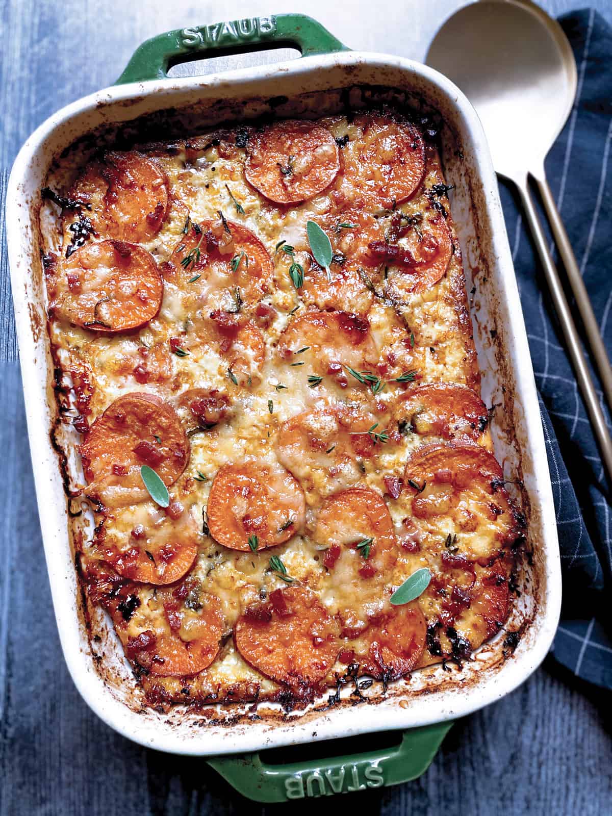 A baking pan with sweet potato au gratin and two gold serving utensils.