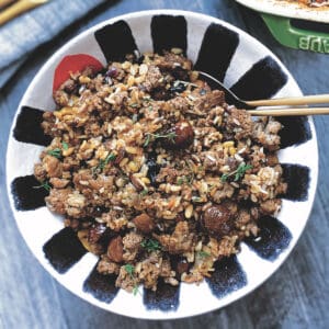 A bowl with turkey stuffing and two gold serving utensils.