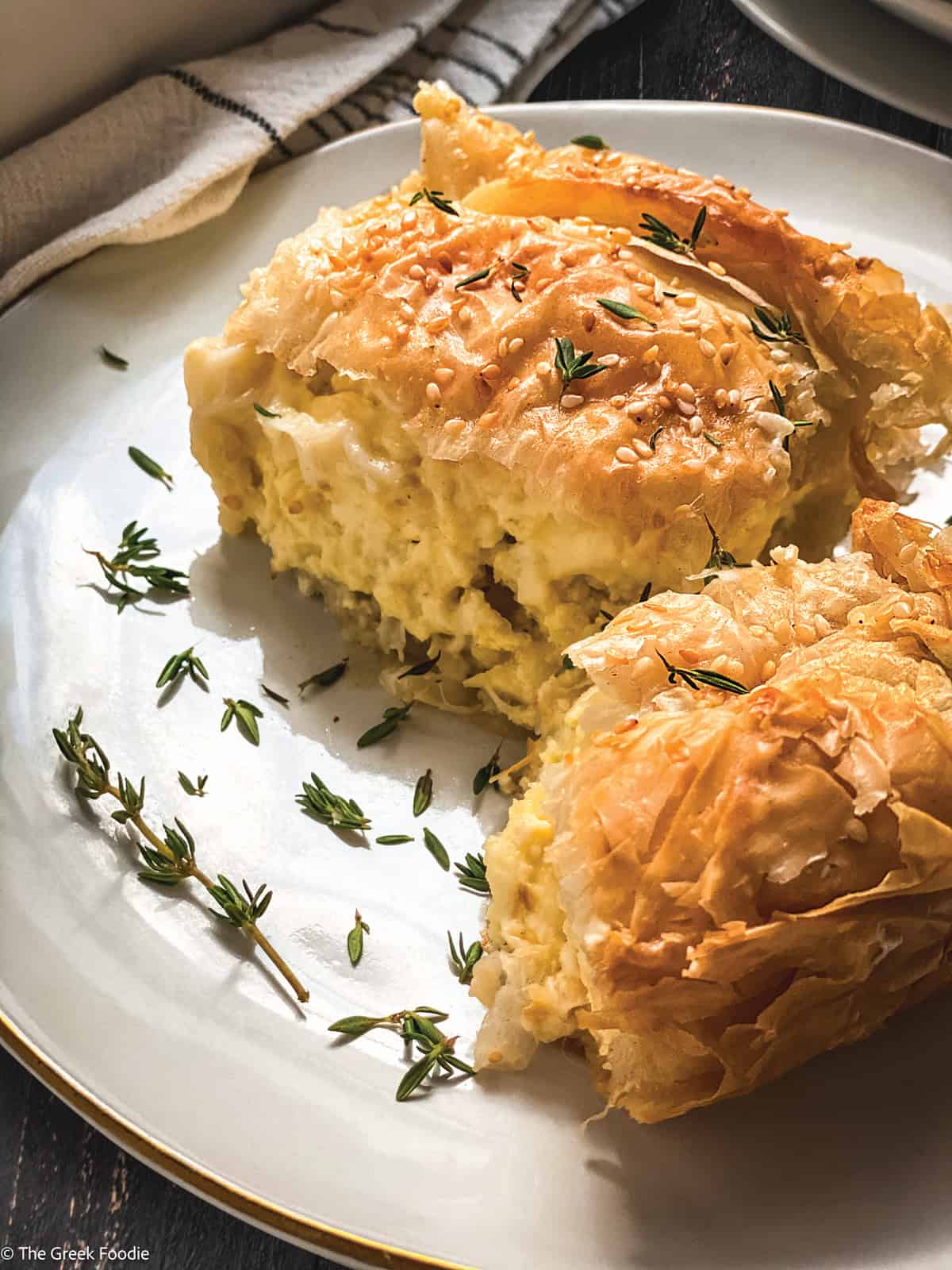 A white baking pan with Greek cheese pie-tiropita, serving utensils and a cloth napkin.