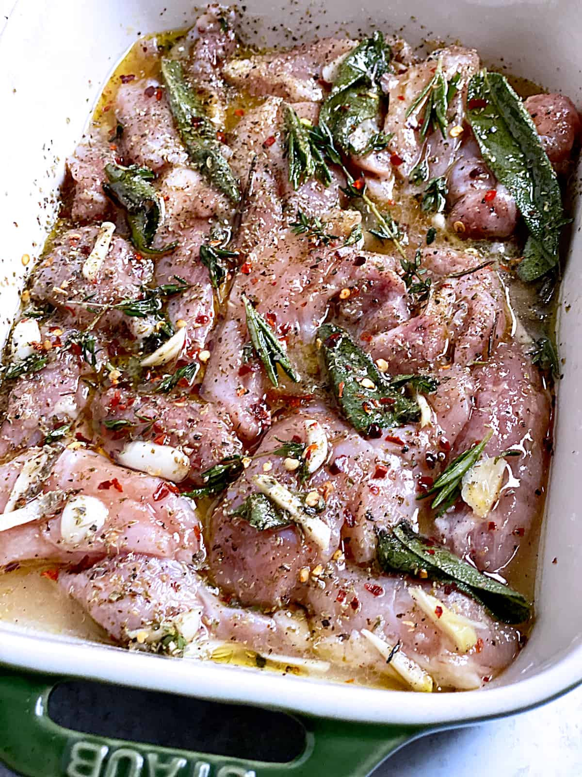Chicken marinating in a pan with fresh herbs and spices.