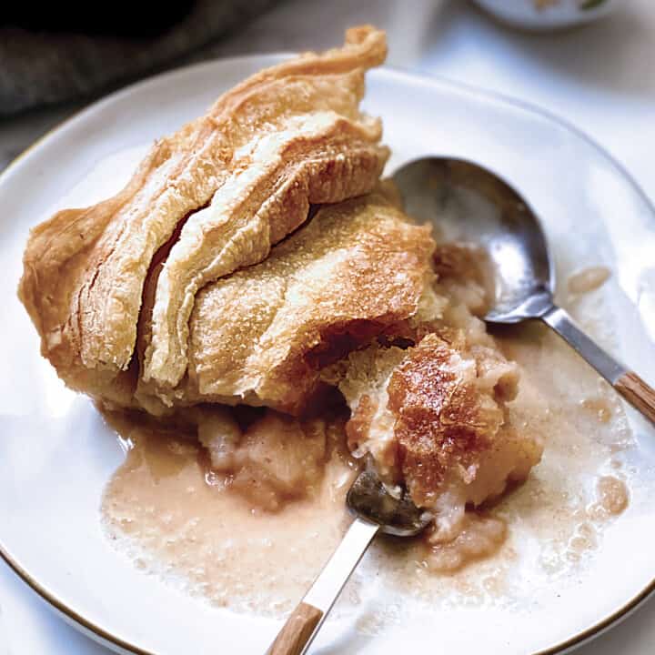 A piece of apple pie on a plate with a fork and spoon.