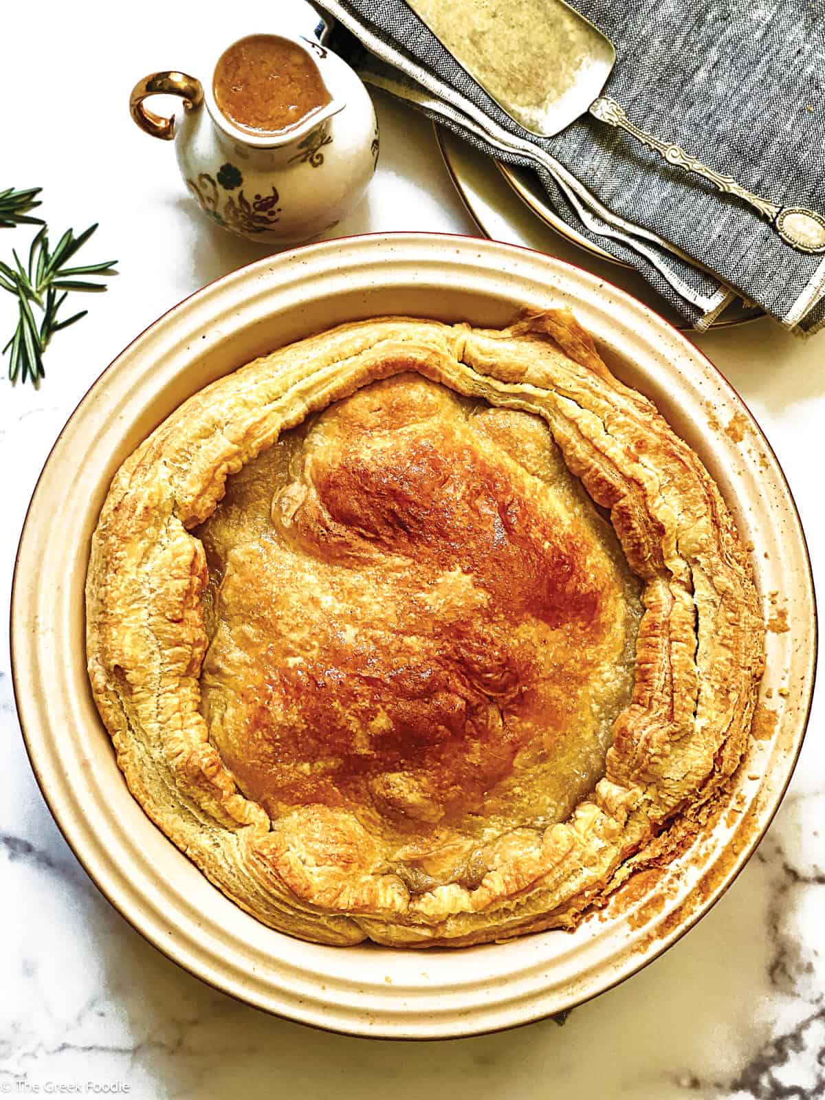 An apple pie in a round tart pan, a canister with sauce, naplins and serving utensils.