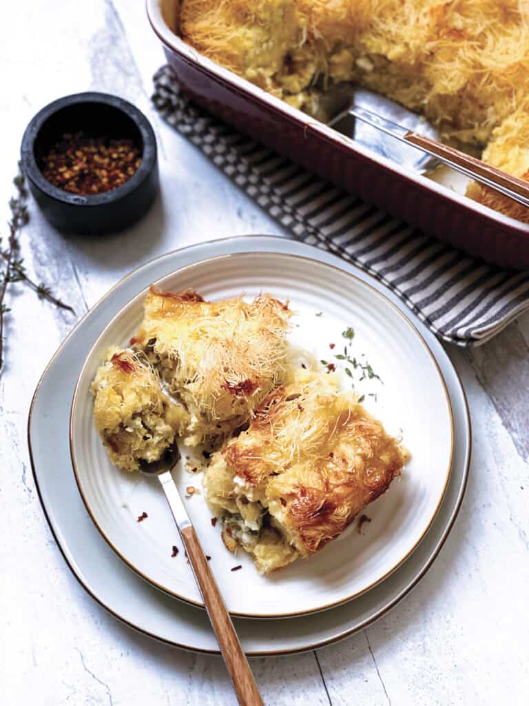 Two pieces of cheese pie on a plate with utensils, a baking pan at the back.