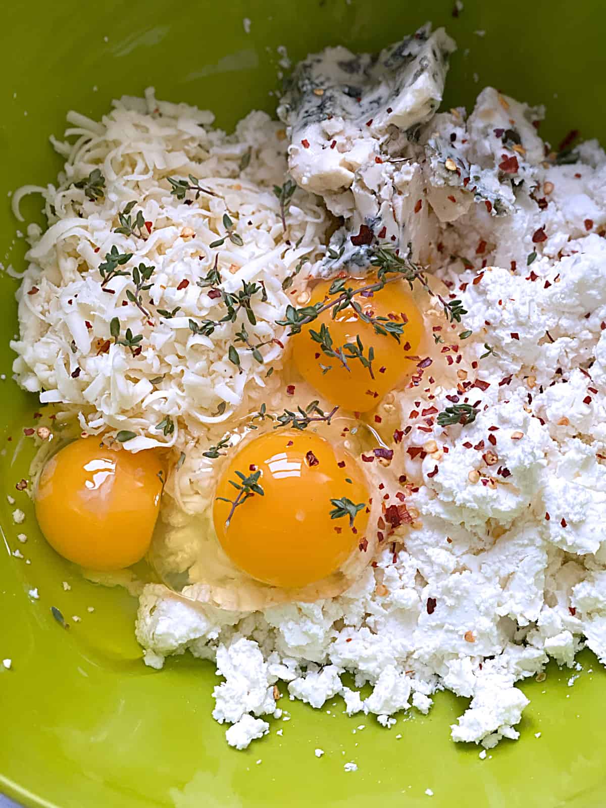 A green bowl with crumbled cheese, eggs and seasonings.