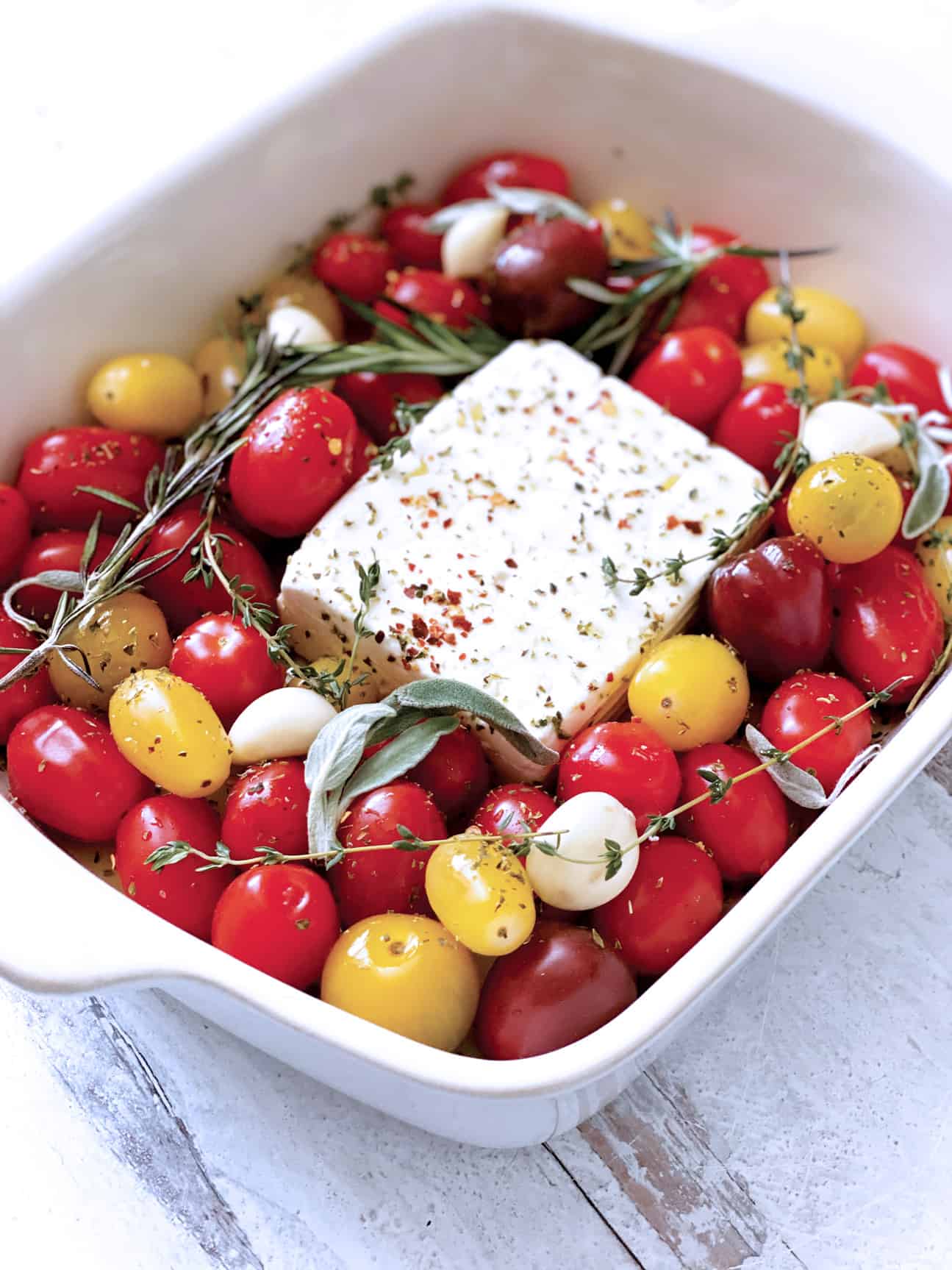 A baking pan with cherry tomatoes and a block of feta cheese in the middle.