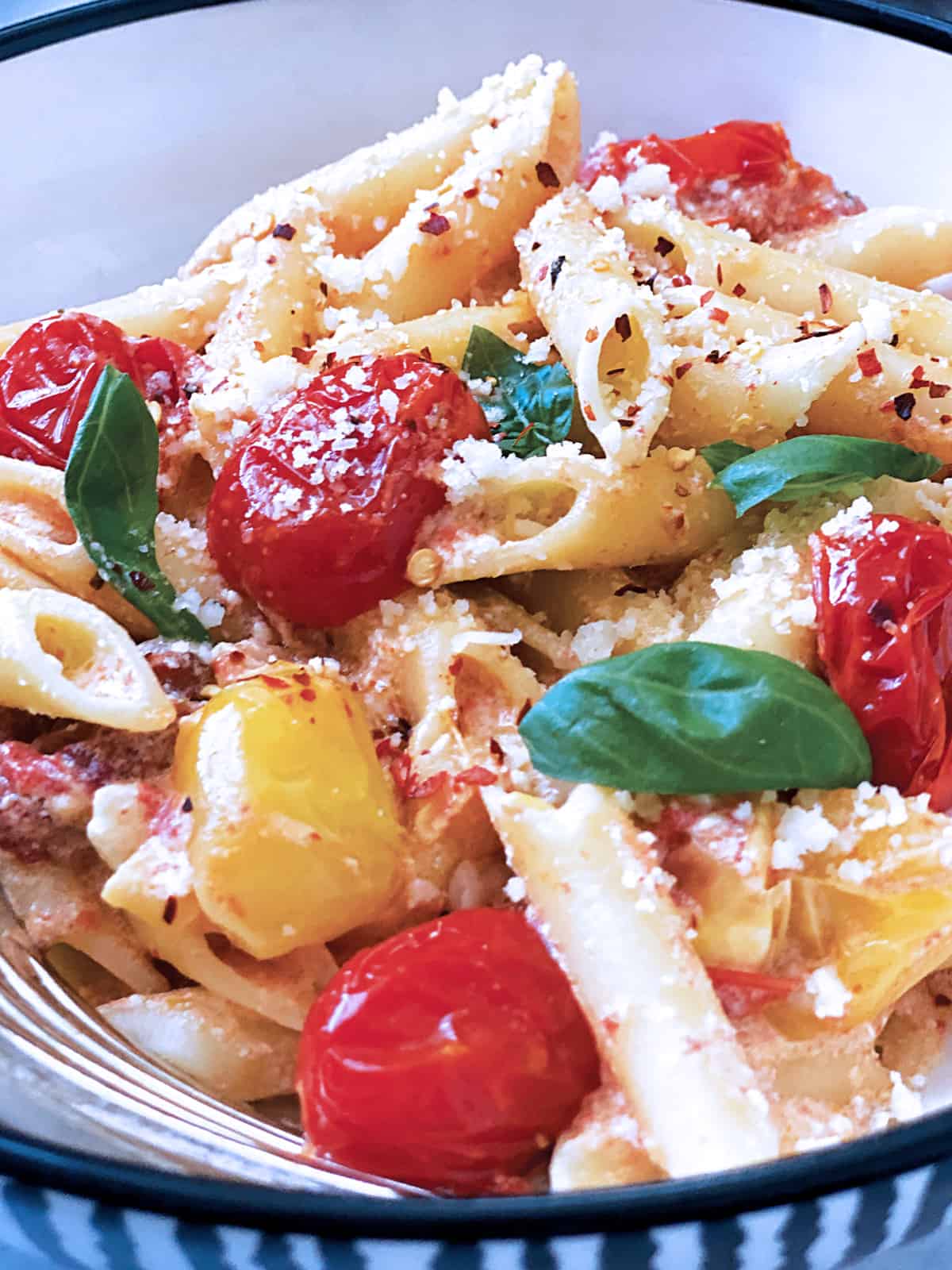 A plate with pasta with tomatoes and feta and fresh basil.