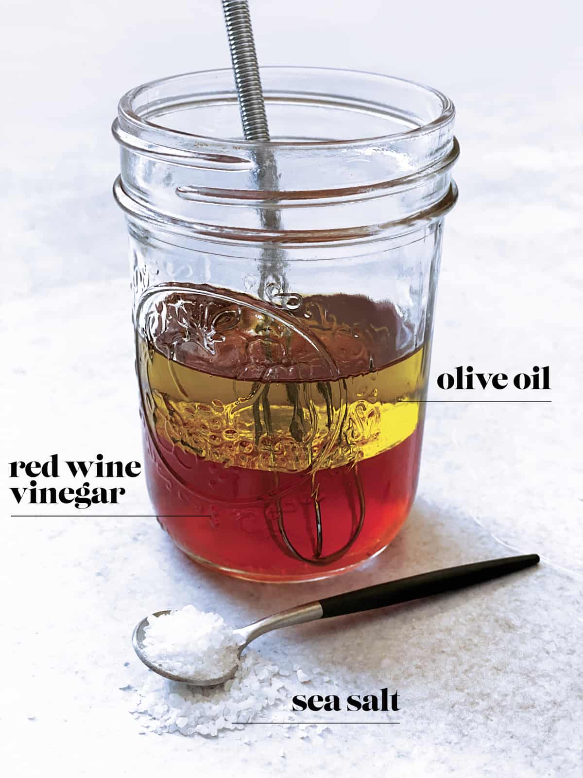A glass with olive oil, red wine vinegar and a spoon with coarse sea salt.