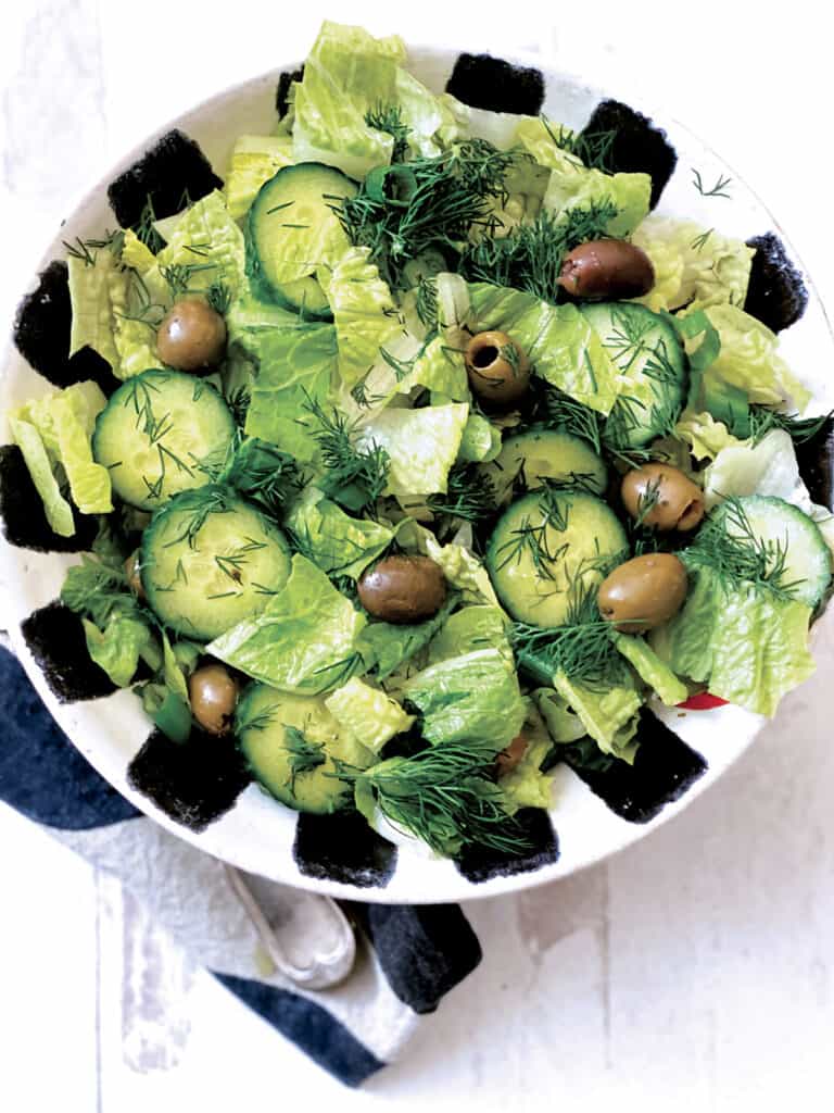 A bowl with greek green salad-maroulosalata, on a cloth napkin.