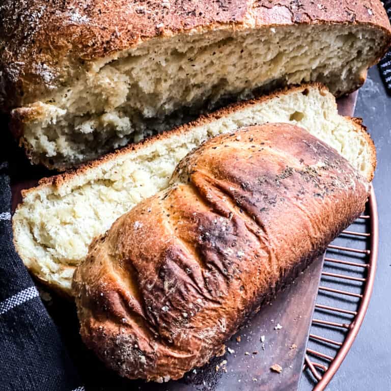 A loaf of bread with two slices cut on a wired copper surface.