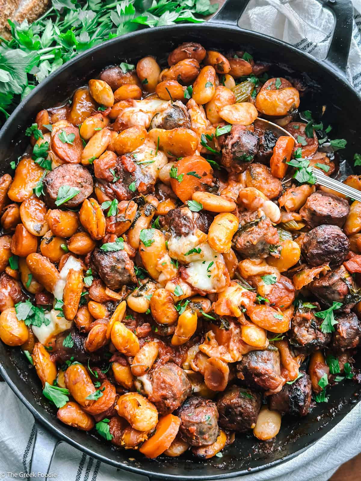 Gigantes plaki with sausage and graviera cheese in a cast iron skillet