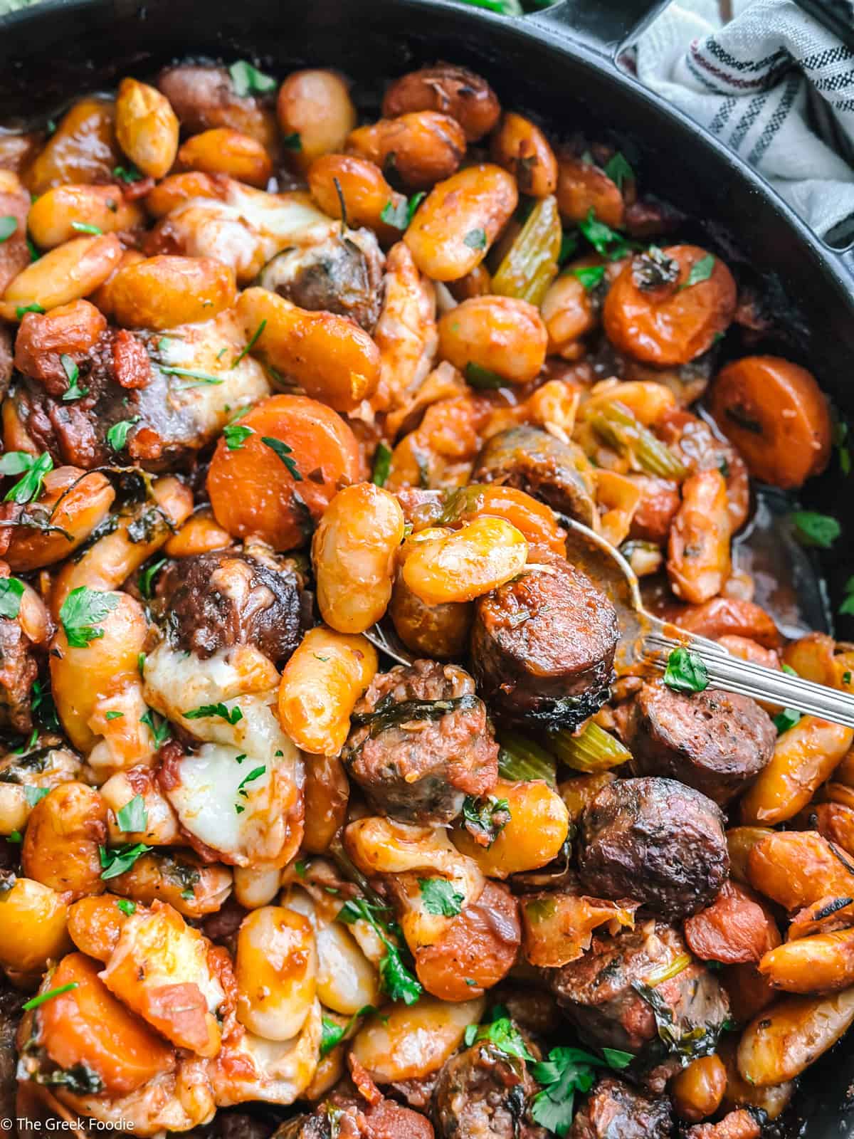 Cast iron skillet with gigantes plaki, fresh parsley, and graviera cubes