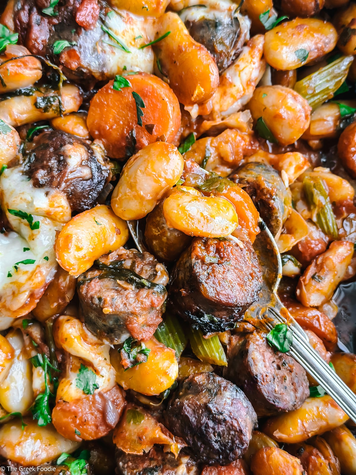 Overhead view of gigantes plaki with carrots, sausage, and cheese in a skillet
