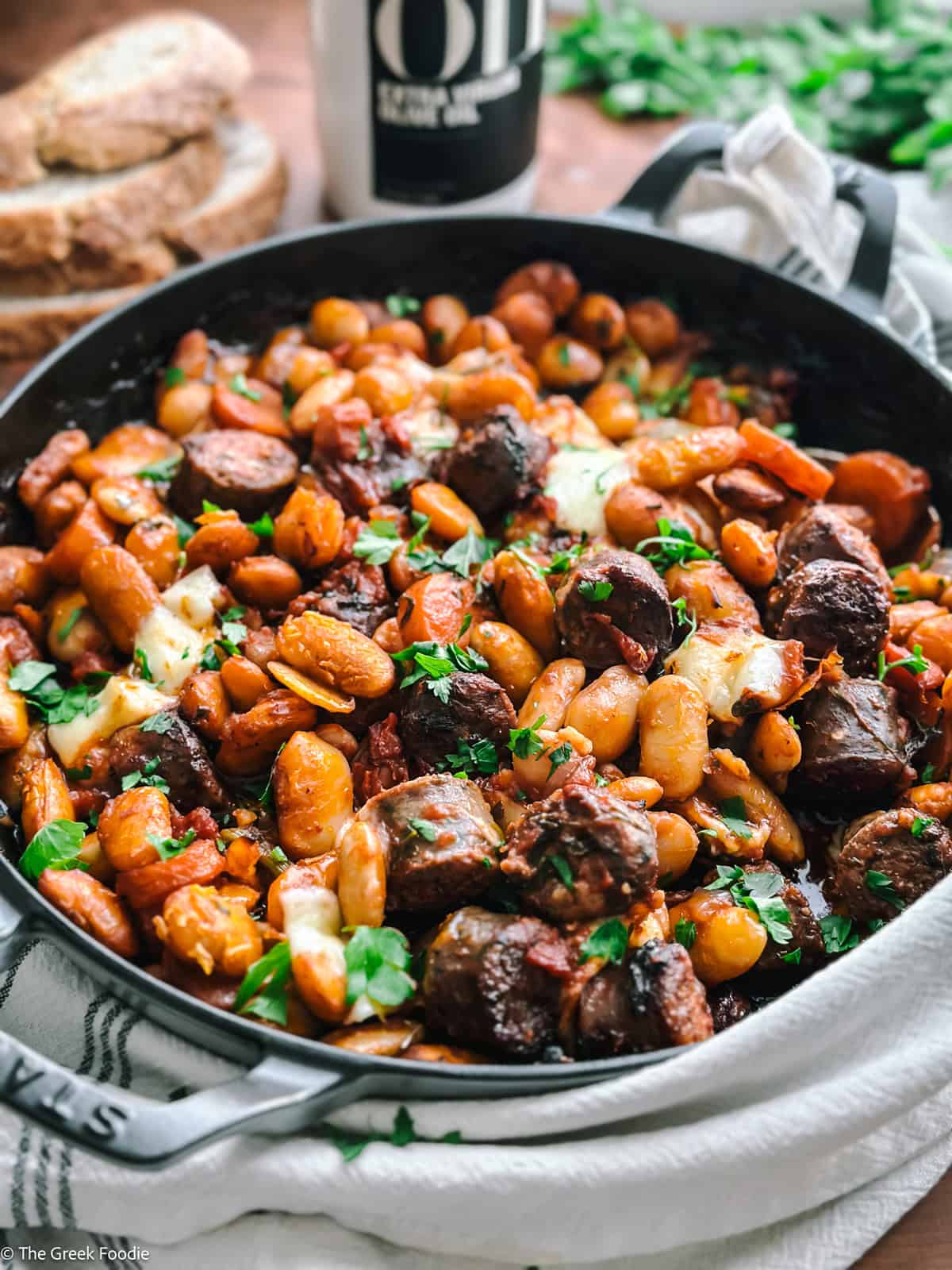 Gigantes plaki in a cast iron pan with bread and olive oil in the background