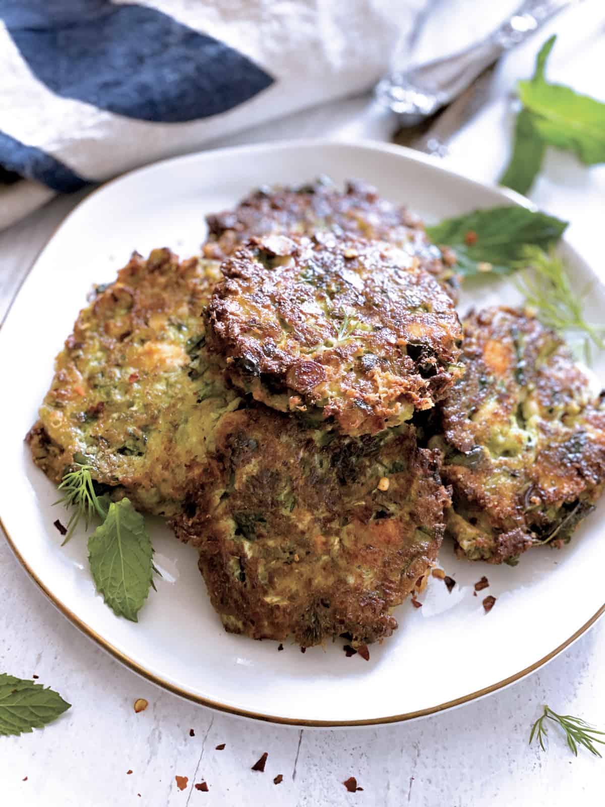 A plate with zucchini patties, utensils and a cloth napkin at the back.