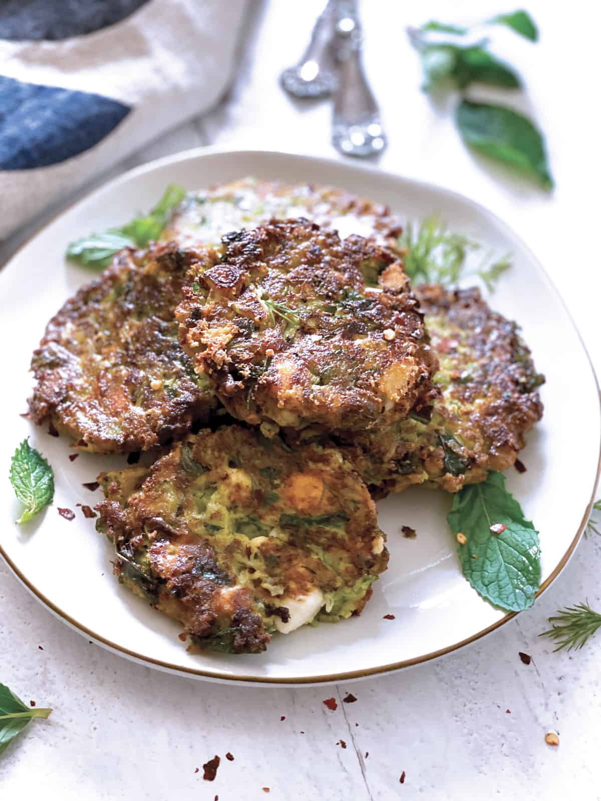 A plate with zucchini patties, utensils and a cloth napkin at the back.