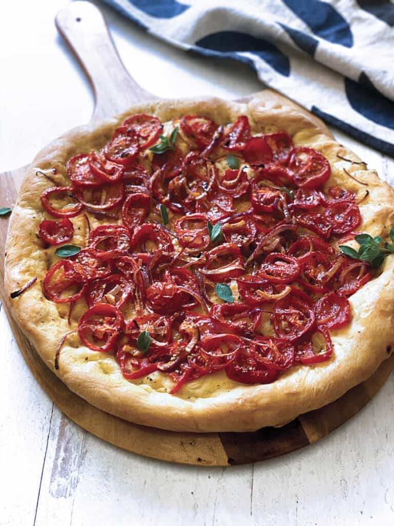 A Ladenia-vegan greek pizza on a pizza peel and a cloth napkin.