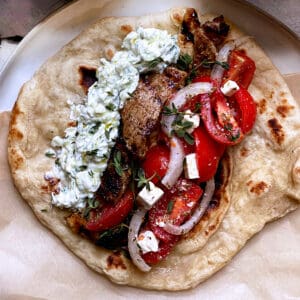 A pita bread with pork, tzatziki, tomatoes and onions.