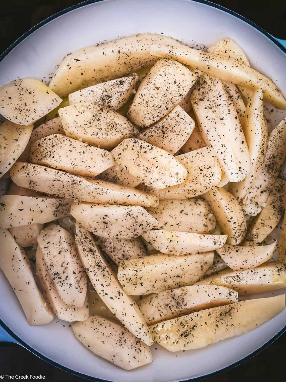 Raw potatoes with herbs in a pan for making Greek spatchcocked chicken