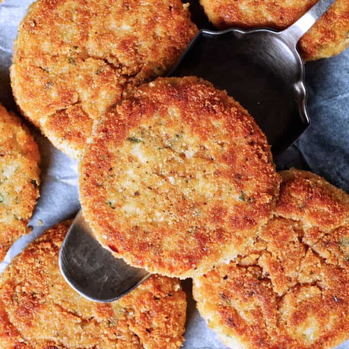 Codfish cakes on parchment paper. One on a serving utensil.