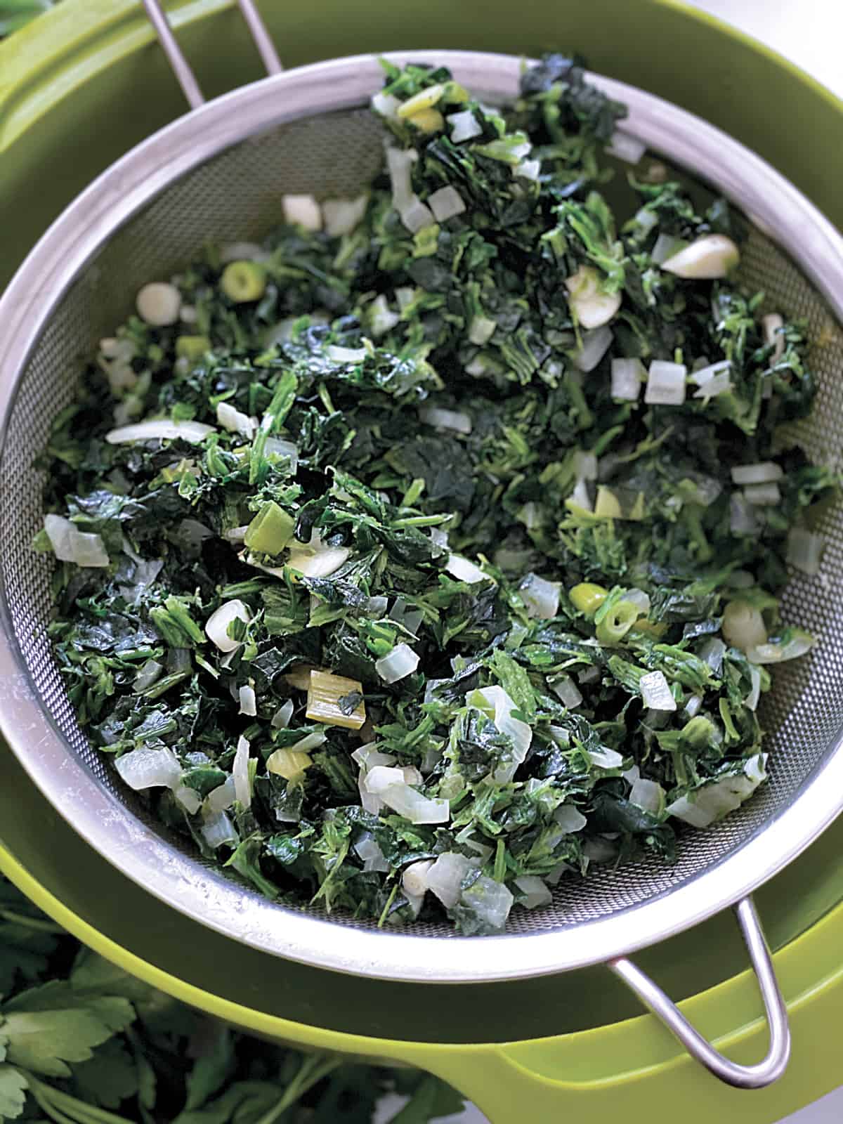 Diced onion, spinach and scallions in a  colander and a green bowl.